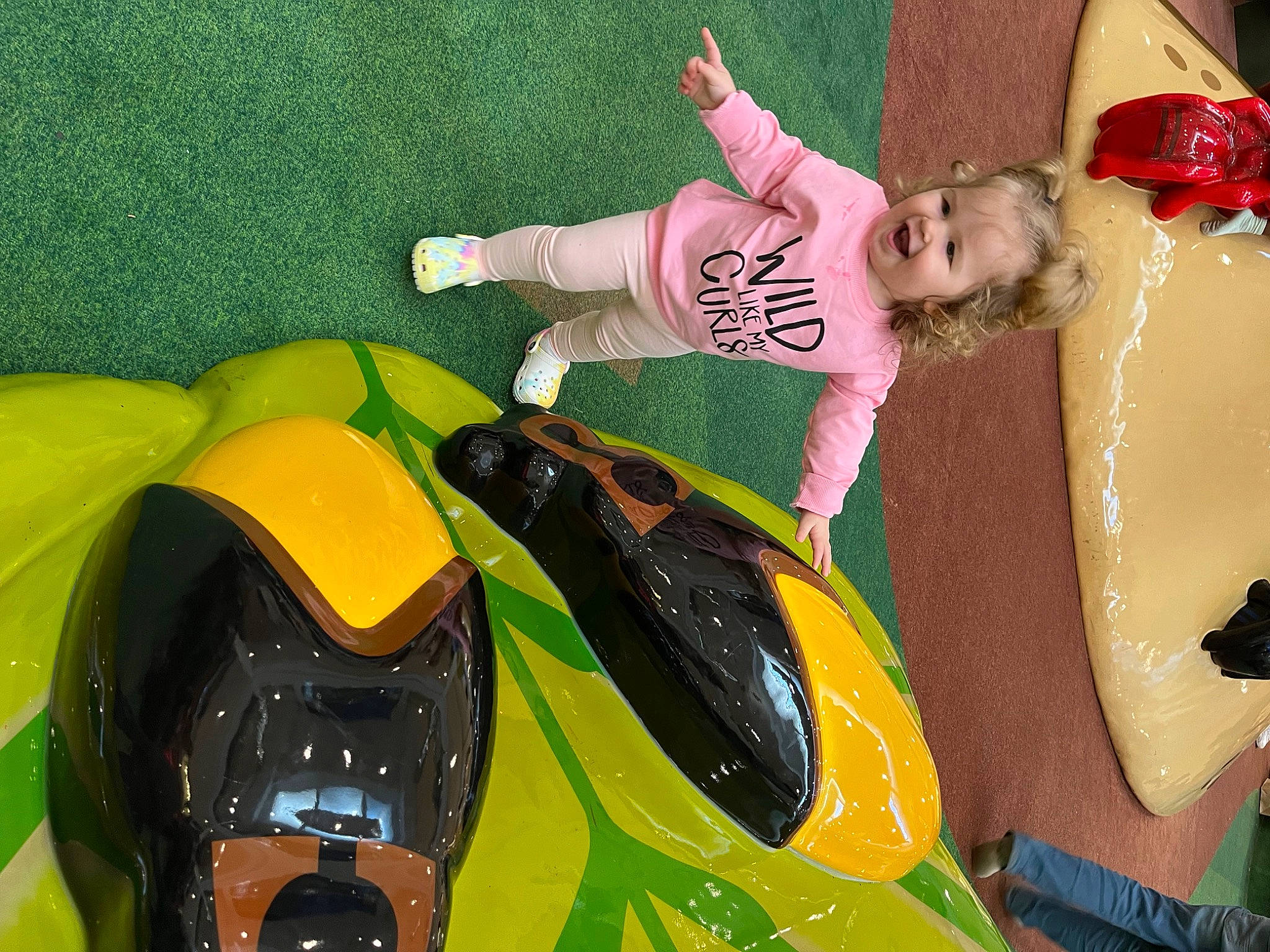 Bella is registered to the contest to win money with this photo: automotive_design, automotive_exterior, bumper, car, fun, grass, happy, hood, leisure, motor_vehicle, person, personal_protective_equipment, play, recreation, riding_toy, smile, sports_car, toddler, toy, toy_vehicle