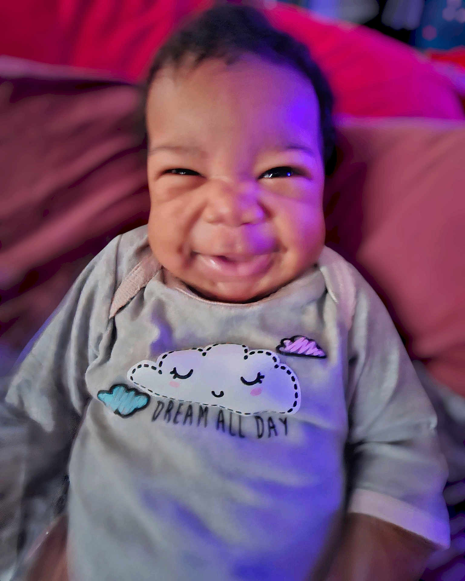 Amira is registered to the contest to win money with this photo: baby, infant, smiling, face, clothing, pillow, purple_light, indoor, cute, happy, portrait, sitting, child, soft_toys, cozy, dream, long_sleeve, expression, closeup, candid