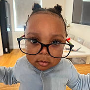 Oziah Omoniyi joined the competition — help win amazing prizes! toddler, child, glasses, indoors, curious, face, hair_buns, long_sleeve, person, portrait, young_child, expression, magnified_eyes, home, table, chair, window, floor, light, casual_clothing