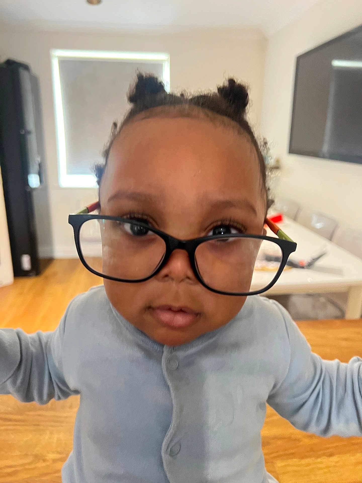 Oziah Omoniyi joined the competition — help win amazing prizes! toddler, child, glasses, indoors, curious, face, hair_buns, long_sleeve, person, portrait, young_child, expression, magnified_eyes, home, table, chair, window, floor, light, casual_clothing