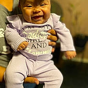 Abigail is registered to the contest to win money with this photo: baby, blurred_background, bow, child, cute, fashion, hand, happy, headwear, holding, indoor, infant, person, portrait, purple_clothing, ribbed_texture, sitting, smiling, toddler, young_child