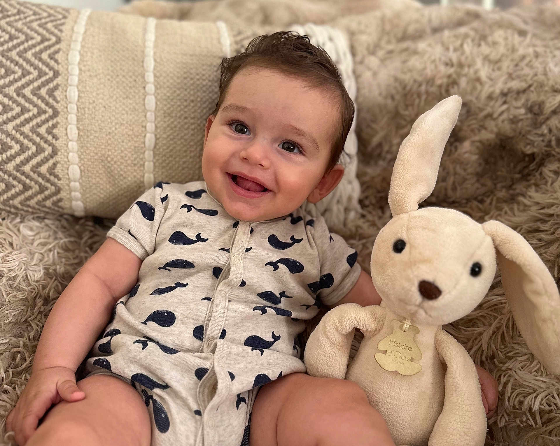 Mathéo participe au concours pour gagner de l'argent avec cette photo : baby, child, smiling, onesie, whale_pattern, stuffed_bunny, plush_toy, blanket, pillow, cozy, indoor, cute, happy, portrait, soft_toy, infant, candid, seated, comfort, home