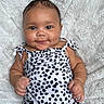 arms, baby, blanket, child, cute, face, happy, indoors, infant, legs, lying_down, onesie, patterned_clothing, person, portrait, skin, smiling, soft_texture, toddler, young