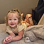 toddler, child, smiling, curly_hair, blue_eyes, bed, blanket, indoor, soft_texture, clothing, happy, person, portrait, couch, furniture, cute, baby, relaxed, plush, light