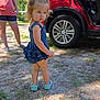 toddler, child, blue_dress, shoes, grass, dirt, car, red_car, open_car_door, woman, casual_clothing, trees, sunlight, shadow, outdoor, daytime, person, nature, serious_expression, standing
