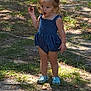 toddler, child, outdoor, grass, sunlight, shadow, blue_romper, pigtails, footwear, crocs, expression, holding, grass_patch, dirt, daylight, person, young_child, cute, small_object, nature