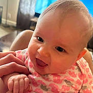 Lilith joined the competition — help win amazing prizes! baby, infant, child, smiling, happy, portrait, close_up, indoors, family, adult_hand, hand, fingers, onesie, pink_clothing, patterned_clothing, television, living_room, warm_lighting, face, photography