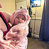 baby, infant, child, portrait, pink, blanket, hood, bow, bundled, wide_eyed, face, eyes, adult, holding, indoor, home, living_room, lamp, curtain, family