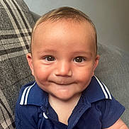 Oakley joined the competition — help win amazing prizes! baby, child, smile, face, eyes, shirt, blue_clothing, couch, plaid_pillow, indoor, person, cute, infant, portrait, young_child, sitting, happy, skin, head, expression