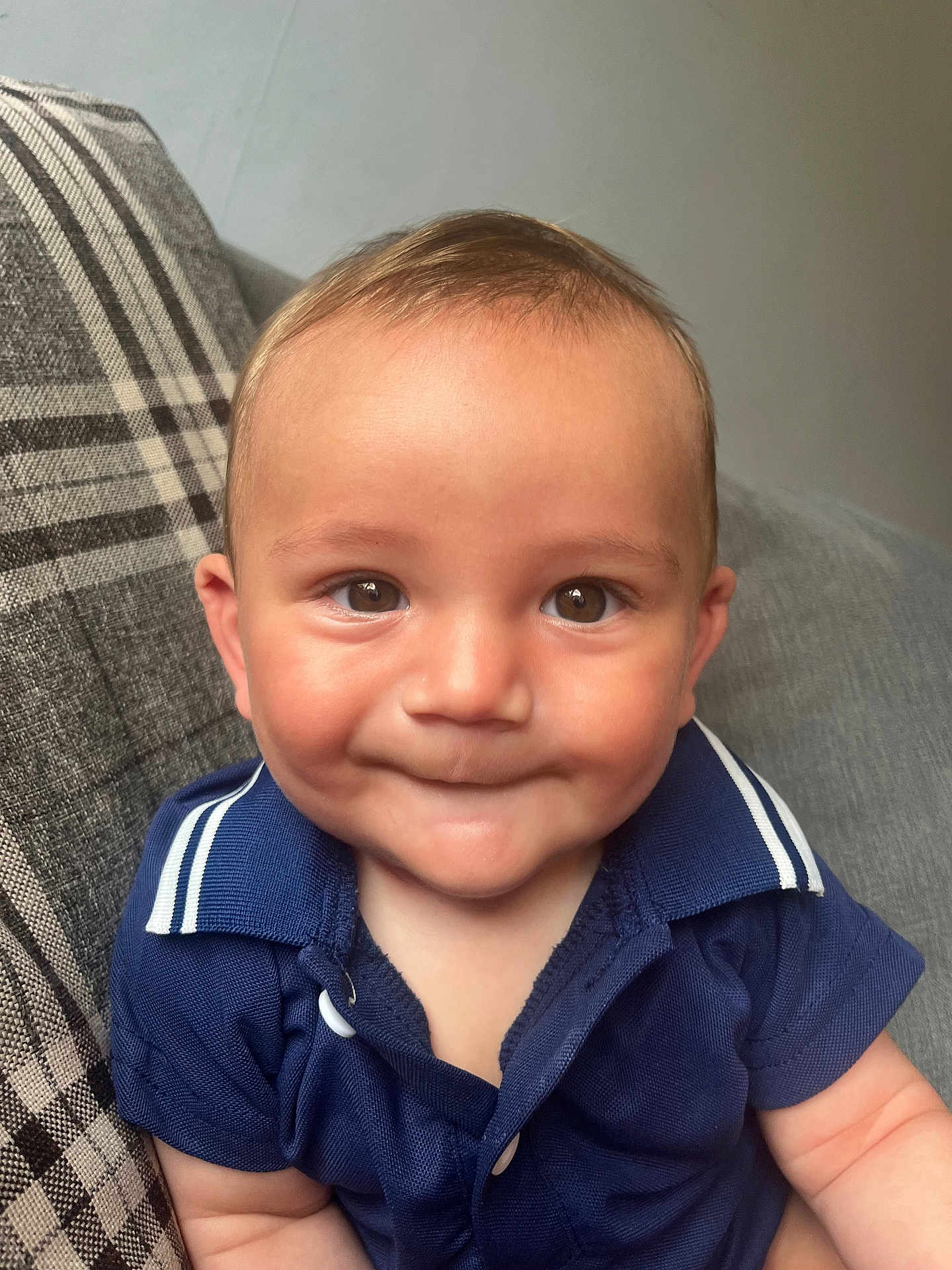 Oakley joined the competition — help win amazing prizes! baby, child, smile, face, eyes, shirt, blue_clothing, couch, plaid_pillow, indoor, person, cute, infant, portrait, young_child, sitting, happy, skin, head, expression