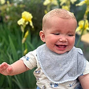Stetson is registered to the contest to win money with this photo: baby, smiling, child, outdoor, greenery, flowers, yellow_flowers, purple_flowers, bib, happy, infant, portrait, grass, nature, cute, toddler, young_child, person, garden, daylight