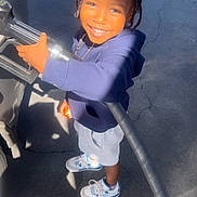 Kayden joined the competition — help win amazing prizes! child, smiling, braids, gas_pump, gas_station, hoodie, shorts, sneakers, asphalt, sunlight, outdoor, person, young_child, casual_clothing, standing, daytime, happy, portrait, holding, bright