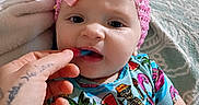 Krimson is registered to the contest to win money with this photo: baby, bed, blanket, child, colorful_clothing, curious, cute, expression, feeding, food, hand, headband, indoor, infant, person, pink_bow, portrait, skeleton_print, tattoo, tropical_print