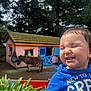 Erick is registered to the contest to win money with this photo: child, toddler, blue_shirt, smiling, outdoor, playhouse, donkey, greenery, hand, person, sunlight, trees, grass, animal, daytime, happy, cute, face, nature, fun