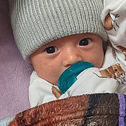 Jesus joined the competition — help win amazing prizes! baby, infant, pacifier, knitted_hat, blanket, sleepwear, closeup, face, eyes, cute, child, indoors, cozy, soft_texture, wearing, portrait, warm, resting, newborn, comfort