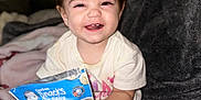 Amelia joined the competition — help win amazing prizes! baby, child, smile, snack, food, package, blanket, sitting, indoors, cute, happy, toddler, clothing, person, face, hand, furniture, soft, comfort, playful