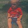 child, boy, grass, outdoor, sunny, red_shirt, blue_shorts, blond_hair, sitting, backyard, house, trees, daylight, casual_clothing, barefoot, person, portrait, nature, summer, leisure
