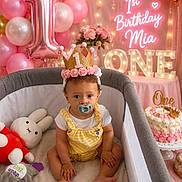 Aurelie is registered to the contest to win money with this photo: baby, balloons, birthday, cake, celebration, child, crown, decorations, first_birthday, flowers, gold, indoors, neon_sign, pacifier, party, pink, playpen, smiling, table, toys