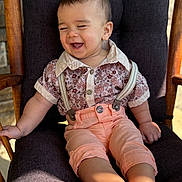 Lucas is registered to the contest to win money with this photo: toddler, child, smiling, shirt, suspenders, pants, barefoot, chair, cushion, wood, indoor, happy, portrait, baby, cute, clothing, person, face, sitting, sunlight
