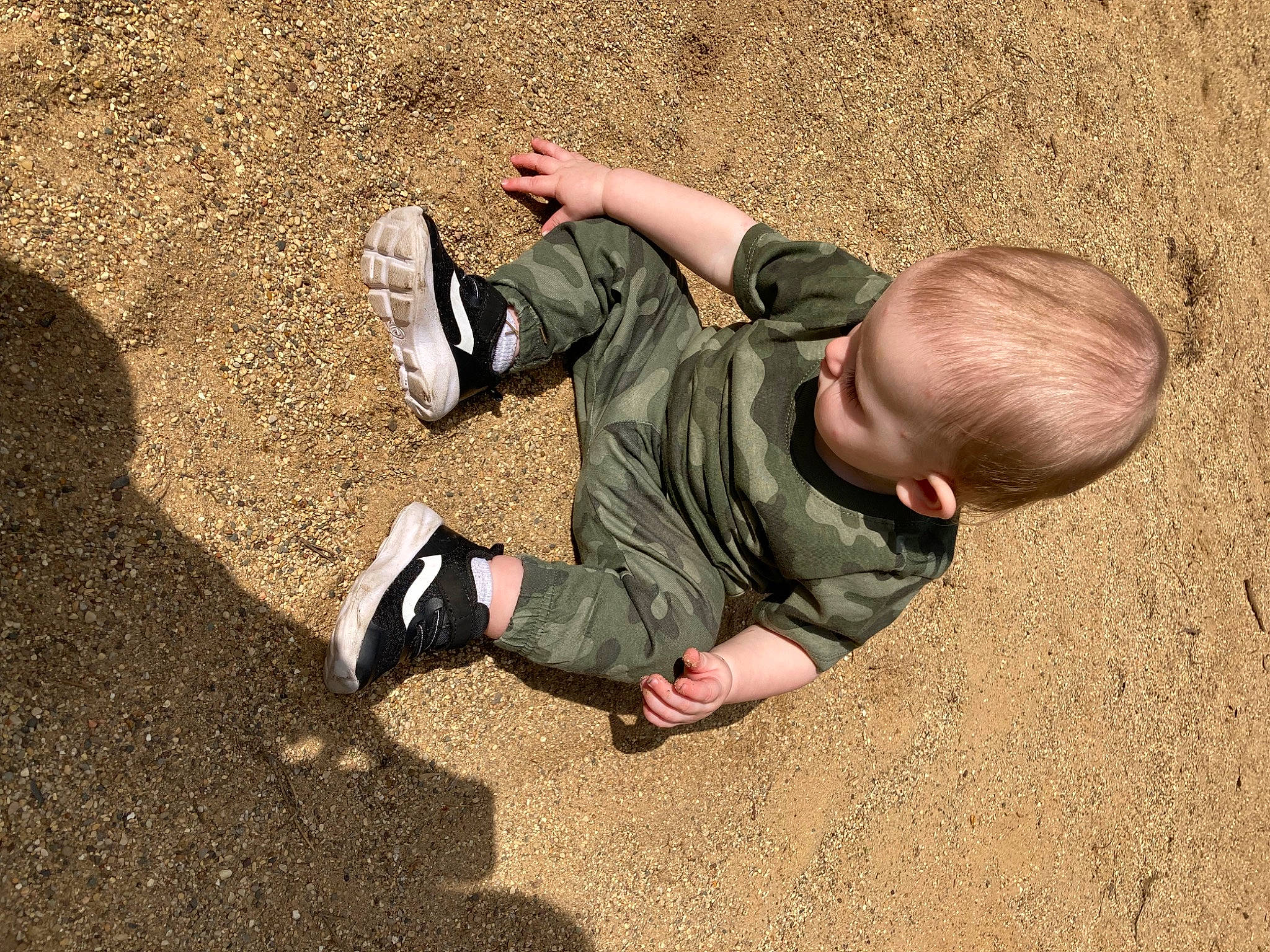 Karson is registered to the contest to win money with this photo: asphalt, flooring, foot, fun, geology, grass, human_leg, knee, landscape, leg, people_in_nature, person, road_surface, shoe, sitting, sneakers, sock, soil, toddler, walking_shoe