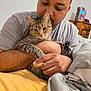Thanos joined the competition — help win amazing prizes! man, cat, indoor, bedroom, tabby_cat, affection, animal, pet, person, furniture, bed, blanket, holding, resting, casual_clothing, closeup, relaxation, comfort, warm_light, home
