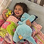 Everleigh joined the competition — help win amazing prizes! toddler, child, bed, crib, quilt, blanket, plush_toy, stuffed_animal, smiling, happy, curly_hair, indoor, sleeping_area, colorful, cute, cozy, person, fabric, toy, resting
