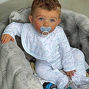 Kayden participe au concours pour gagner de l'argent avec cette photo : baby, child, pacifier, pajamas, armchair, curly_hair, blue_eyes, plush_furniture, indoor, comfort, infant, cute, soft_toys, clothing, sitting, portrait, young_child, baby_bib, relaxed, home