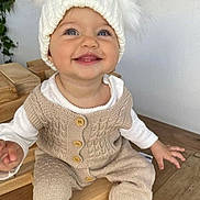 Maïlyna participe au concours pour gagner de l'argent avec cette photo : baby, child, smiling, knitwear, hat, white, cream, wood, happy, sitting, indoor, cute, infant, face, portrait, clothing, button, hand, blue_eyes, cozy