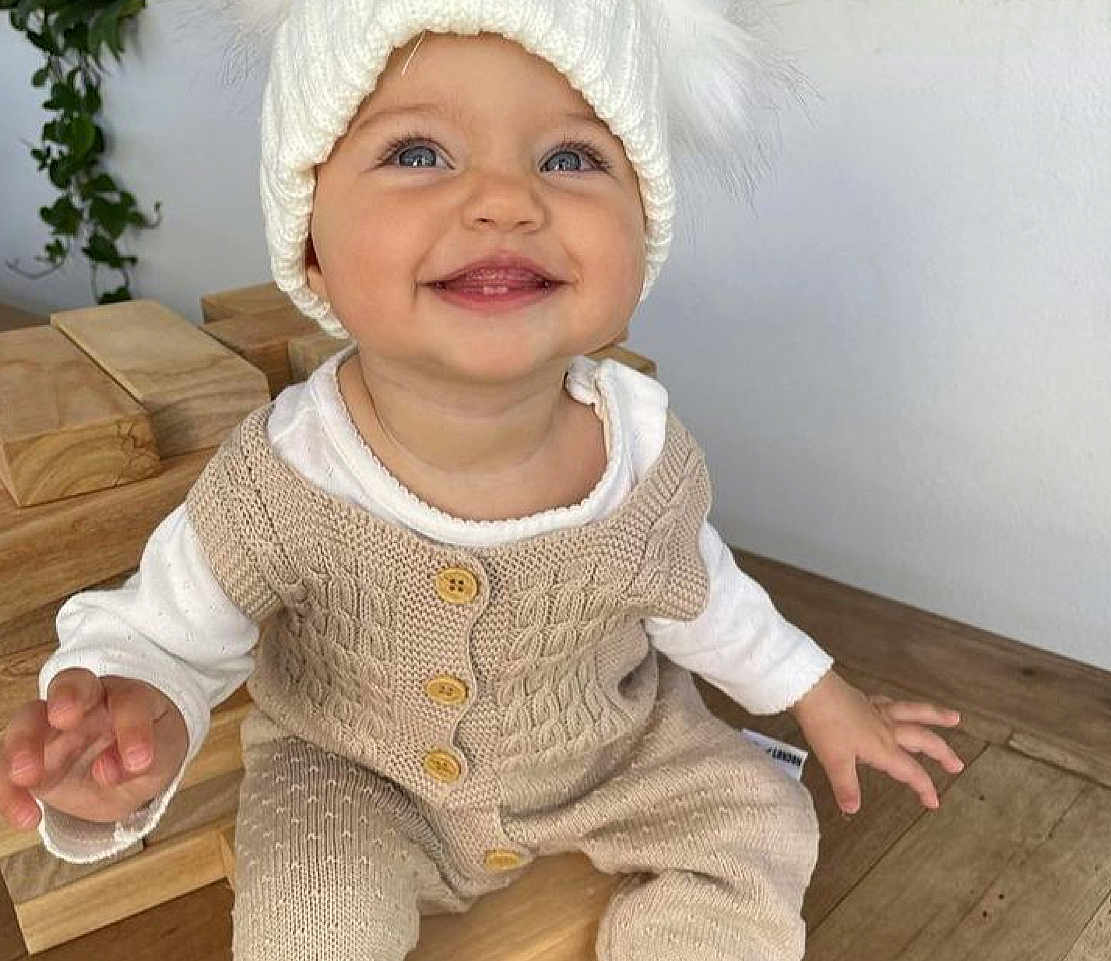 Maïlyna participe au concours pour gagner de l'argent avec cette photo : baby, child, smiling, knitwear, hat, white, cream, wood, happy, sitting, indoor, cute, infant, face, portrait, clothing, button, hand, blue_eyes, cozy