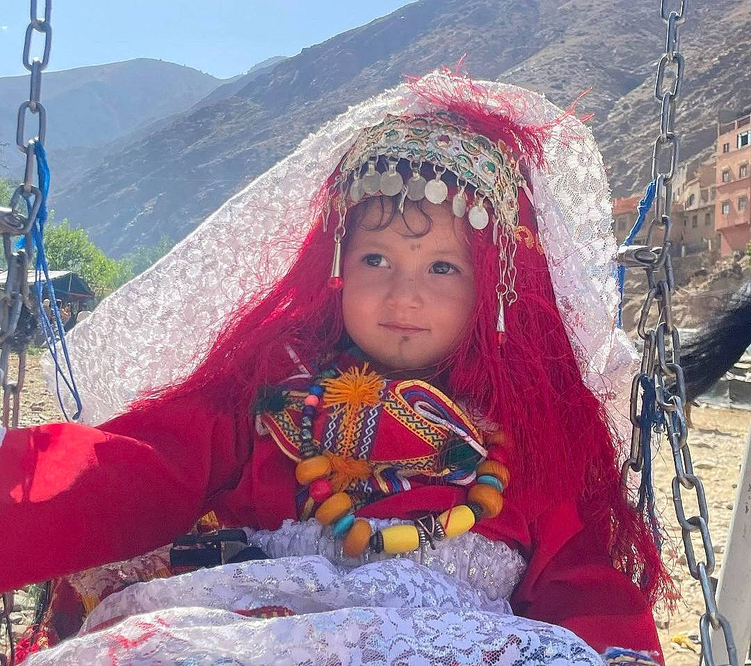 Mayssa participe au concours pour gagner de l'argent avec cette photo : child, event, fun, grass, happy, headwear, landscape, leisure, mountain, mountain_range, people_in_nature, person, recreation, sitting, sky, toddler, tourism, tradition, travel, vacation