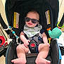 baby, sunglasses, car_seat, bib, smile, indoor, toy, beads, foot, hand, person, reflection, clothing, seat_belt, happy, child, infant, accessory, cute, portrait