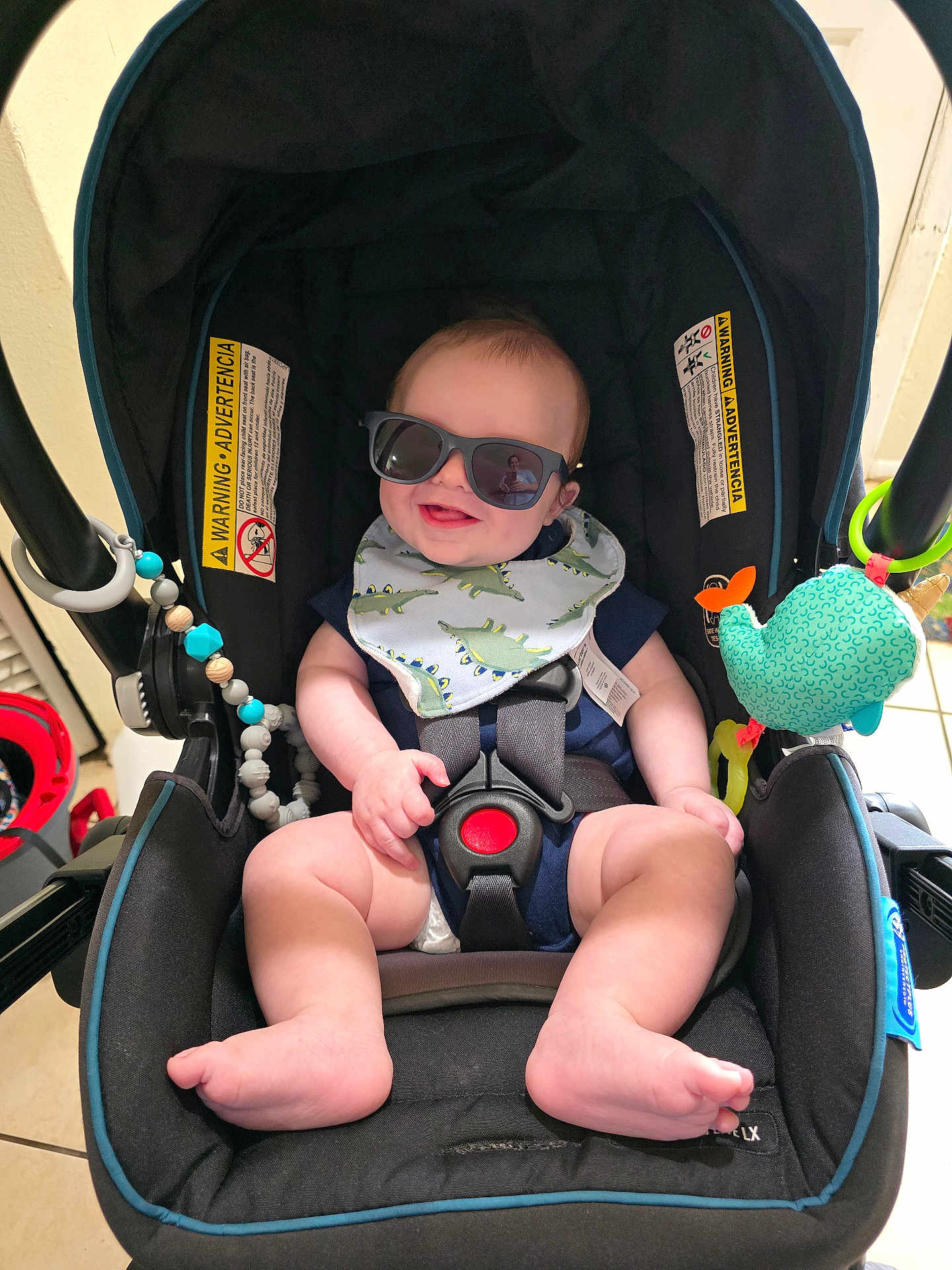 Liam is registered to the contest to win money with this photo: baby, sunglasses, car_seat, bib, smile, indoor, toy, beads, foot, hand, person, reflection, clothing, seat_belt, happy, child, infant, accessory, cute, portrait