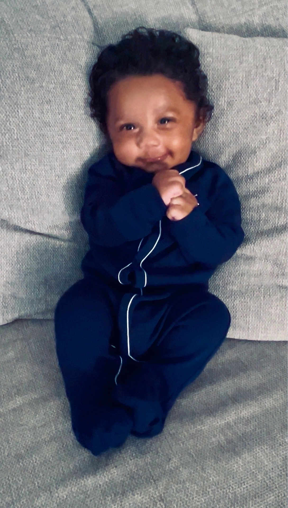 Edwin joined the competition — help win amazing prizes! baby, infant, child, smiling, couch, onesie, clothing, hands, face, happy, sitting, indoor, portrait, cozy, cute, curly_hair, comfortable, texture, sofa, home