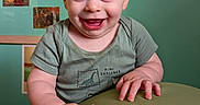 Theo joined the competition — help win amazing prizes! baby, child, infant, smiling, happy, portrait, indoors, green_wall, green_shirt, blue_eyes, seated, hands, table, furniture, home, background, photography, closeup, joyful, playful