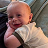 Theo joined the competition — help win amazing prizes! baby, child, infant, smiling, portrait, indoor, living_room, couch, blanket, clothing, white_outfit, sitting, lying_down, face, head, eyes, happy, home, window, daylight