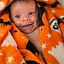 baby, black, blanket, child, closeup, cozy, cute, expression, face, happy, indoors, infant, orange, portrait, smiling, soft, stars, warm, wrapped, young