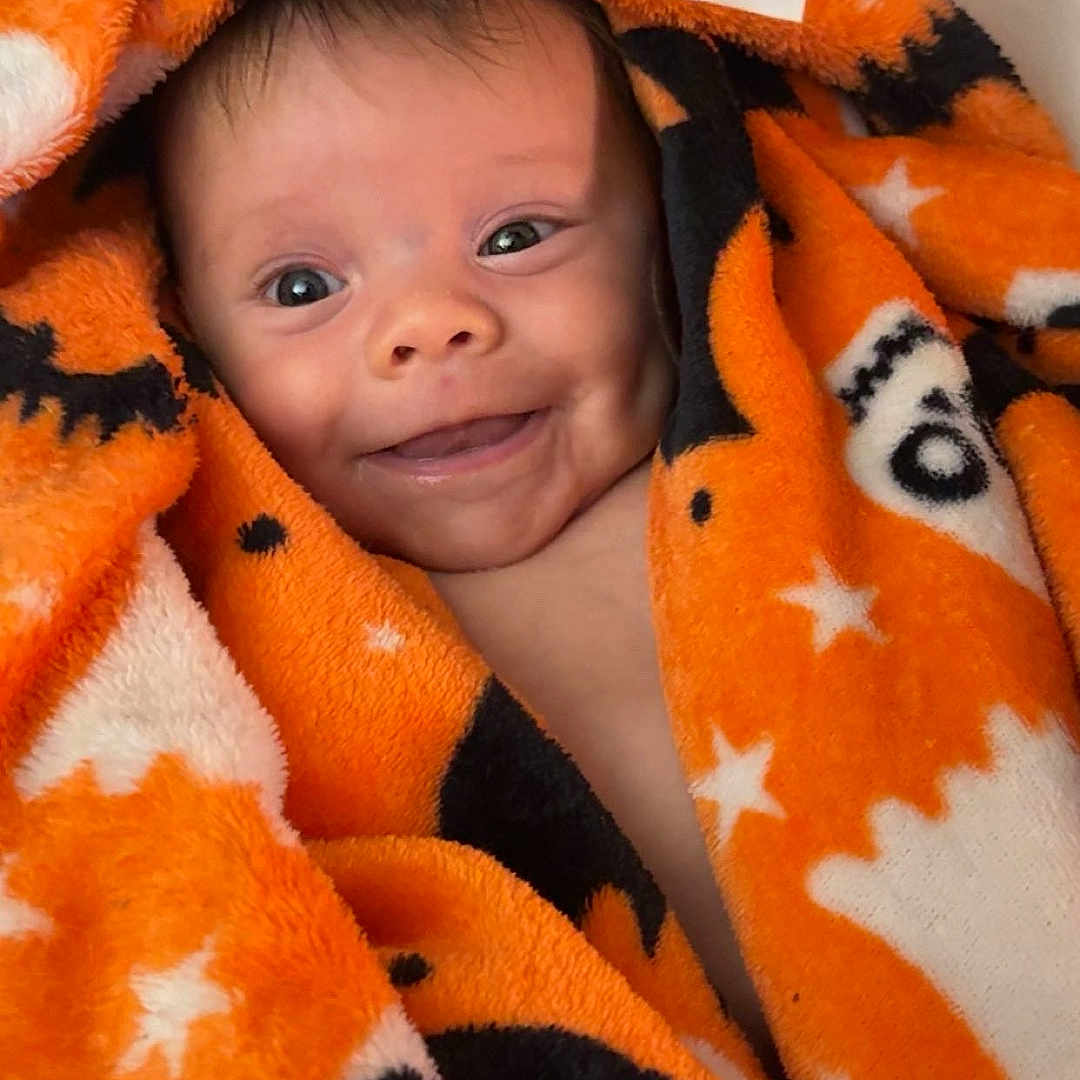 Anya Elaine Pulciani is registered to the contest to win money with this photo: baby, black, blanket, child, closeup, cozy, cute, expression, face, happy, indoors, infant, orange, portrait, smiling, soft, stars, warm, wrapped, young