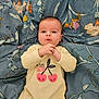 baby, blanket, blue_background, cherry_print, child, clothing, comfortable, cute, expression, face, floral_pattern, hands, indoors, infant, lying_down, onesie, person, portrait, soft, young