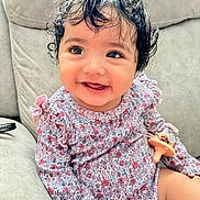 Jaynara Rodas is registered to the contest to win money with this photo: baby, child, infant, smiling, happy, portrait, curly_hair, floral_dress, patterned_clothing, pacifier, sitting, sofa, couch, indoor, close_up, face, eyes, playful, 家庭, photography