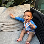 Lucca is registered to the contest to win money with this photo: baby, child, smiling, onesie, sitting, cushion, sofa, outdoor, plant, greenery, happy, infant, furniture, portrait, cute, hand, feet, face, relaxing, cozy