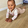 baby, crawling, floor, wooden_floor, indoor, child, smiling, happy, clothing, long_sleeve, baby_gear, baby_rocker, toy, teddy_bear, person, infant, cute, cozy, playful, homedecor