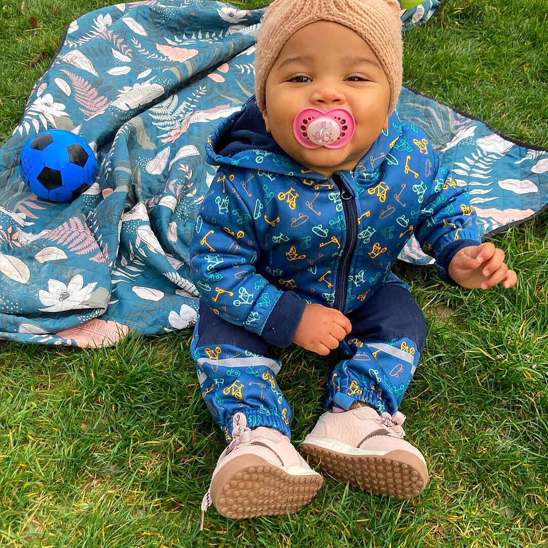 Aline participe au concours pour gagner de l'argent avec cette photo : baby, child, grass, outdoor, pacifier, blue_outfit, knitted_hat, blanket, soccer_ball, sitting, shoes, cute, smiling, play, person, young_child, nature, fun, happy, casual_clothing