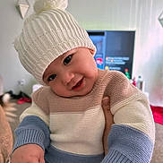 Matteo joined the competition — help win amazing prizes! baby, child, knitted_hat, pom_pom, sweater, striped_clothing, smile, face, hand, indoor, living_room, blurred_background, television, carpet, cozy, cute, person, infant, warm_clothing, portrait