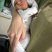 Nicholas is registered to the contest to win money with this photo: baby, infant, pajamas, hat, hand, person, holding, clothing, indoor, cute, newborn, sleepwear, white, green_shirt, face, footwear, whale_pattern, cozy, tender, portrait