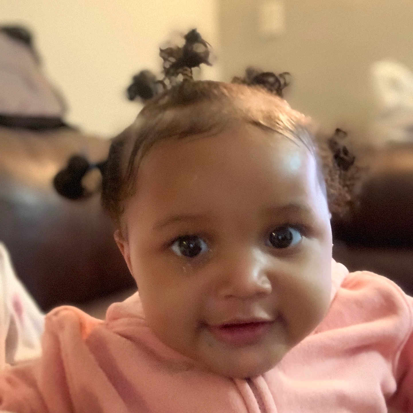 Mahogany joined the competition — help win amazing prizes! adorable, baby, child, closeup, couch, cozy, cute, expression, eyes, face, hair_buns, indoor, infant, person, pink_clothing, portrait, sitting, smile, soft_lighting, young_child