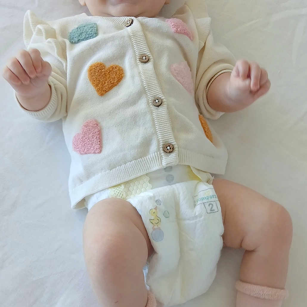 Olyvia a rejoint le concours — aidez-le/la à gagner de superbes lots ! baby, baby_garment, cardigan, child, close_up, clothing, cute, diaper, happy, hearts, indoors, infant, lying_down, person, pink_socks, portrait, smiling, soft_texture, toddler, white_background