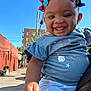 child, toddler, smiling, outdoor, blue_sky, hair_beads, urban, street, holding_hand, clothing, person, happy, daylight, building, sidewalk, tattoo, cute, portrait, baby, casual