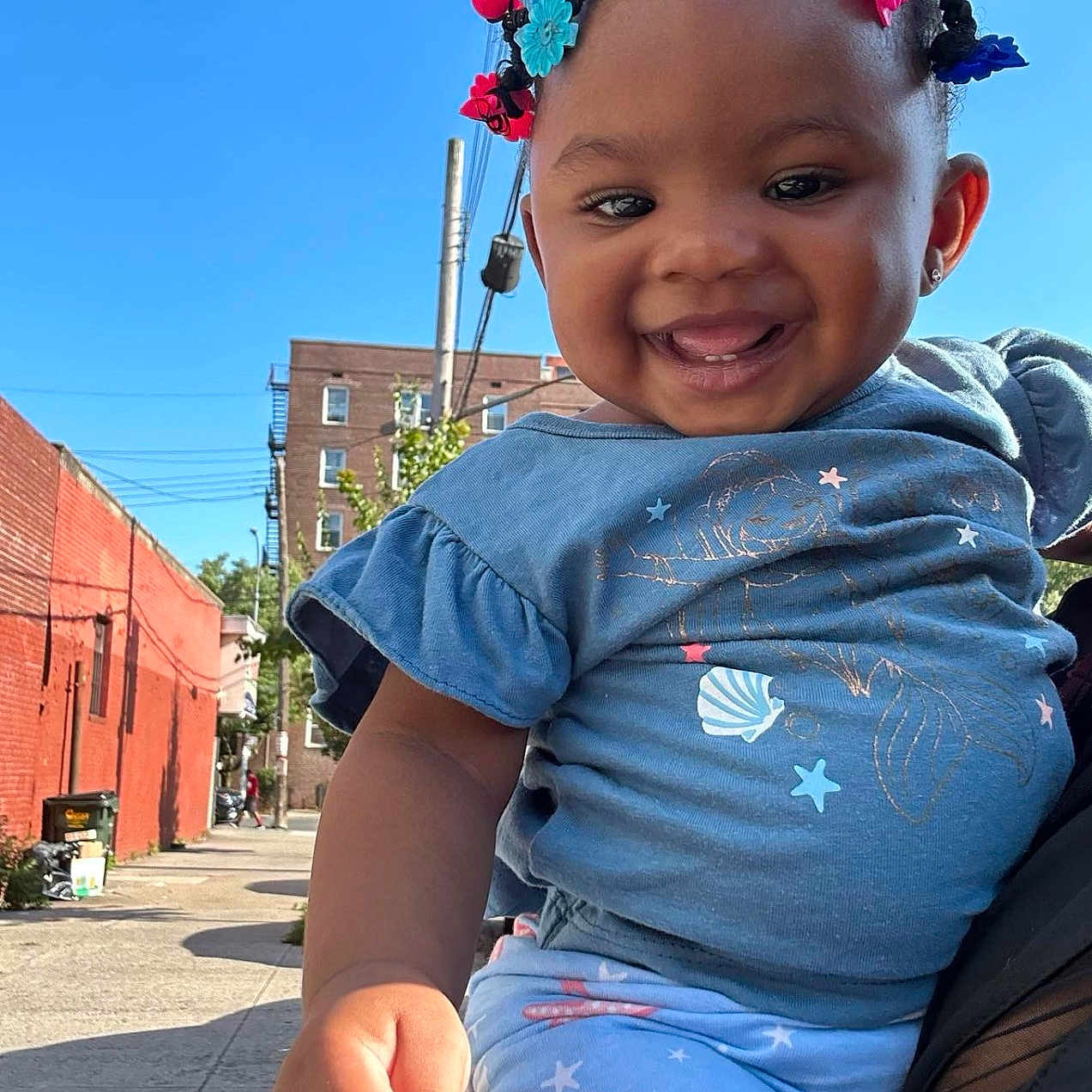 Ta'Sani is registered to the contest to win money with this photo: baby, blue_sky, building, casual, child, clothing, cute, daylight, hair_beads, happy, holding_hand, outdoor, person, portrait, sidewalk, smiling, street, tattoo, toddler, urban