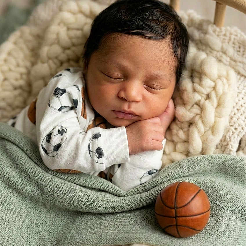 Drixon is registered to the contest to win money with this photo: newborn, baby, sleeping, blanket, knitted, basketball, soccer, outfit, wooden_cradle, cozy, infant, resting, cute, child, portrait, indoor, soft, warm, peaceful, head