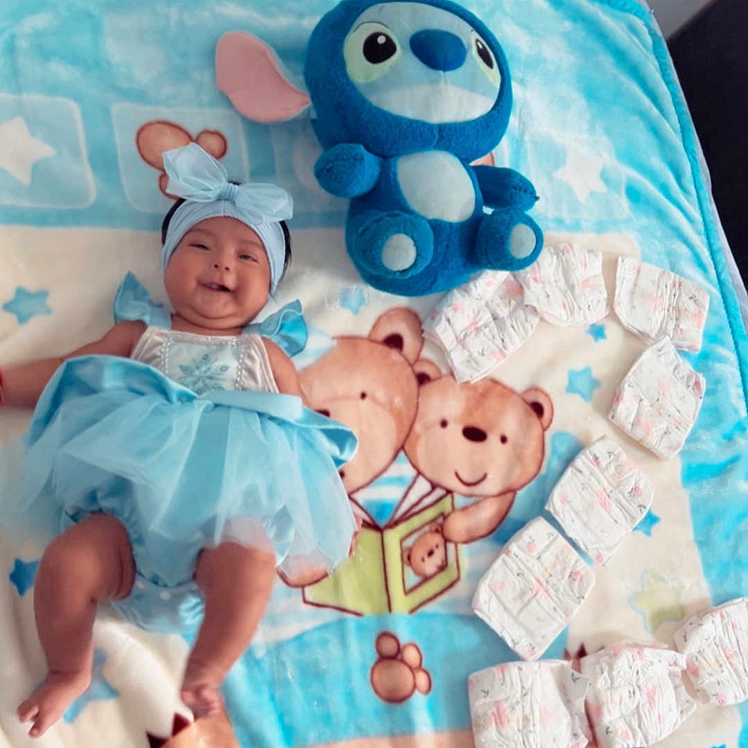 Celeste joined the competition — help win amazing prizes! baby, baby_clothing, bed, blanket, blue_dress, bow, celebration, child, diapers, headband, indoor, infant, lying_down, nursery, photography, playful, portrait, smiling, stitch_plushie, teddy_bears